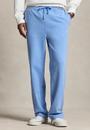 Uomo che indossa pantaloni della tuta azzurri chiaro con coulisse, sneakers bianche e una felpa bianca con orlo a righe.