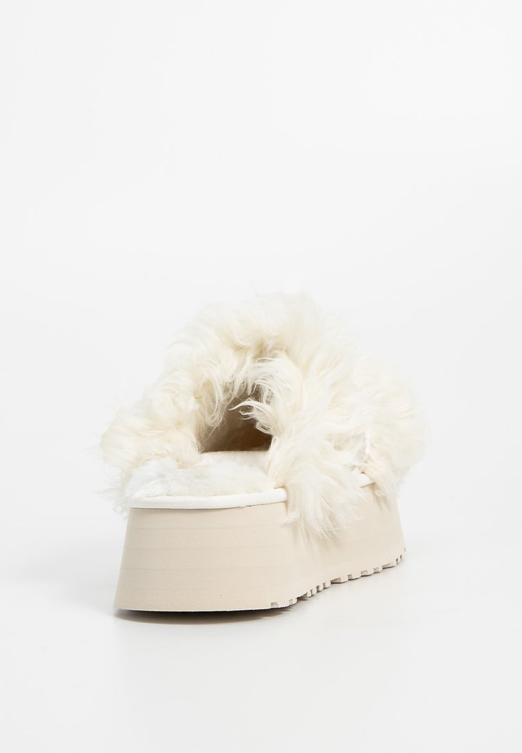 Puszysty biały but wsuwany z grubą beżową platformą, z miękkim, teksturowanym materiałem przypominającym futro wokół kołnierza i wnętrza.
