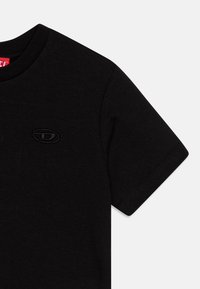 Svart bomull t-skjorte med rund hals og korte ermer, med en hevet svart logo på venstre side av brystet.