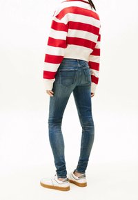 Blauwe skinny jeans gecombineerd met een rood-wit gestreept sweatshirt. De outfit bevat casual witte sneakers met zilveren accenten.