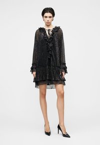 Μαύρο διάφανο φόρεμα με βολάν και δέσιμο στο λαιμό. Διαθέτει μακριά μανίκια, στρώσεις στο τελείωμα και διακριτική λαμπερή υφή.