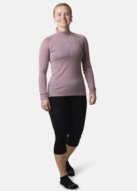 Maglietta a maniche lunghe viola chiaro con zip a metà, abbinata a leggings capri neri. Il tessuto sembra elastico e aderente. Calzini neri alla caviglia.