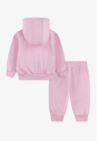 Ροζ βαμβακερή φόρμα που περιλαμβάνει φούτερ με κουκούλα και ριμπ μανσέτες, καθώς και ένα ταιριαστό παντελόνι με ελαστική μέση και μανσέτες.