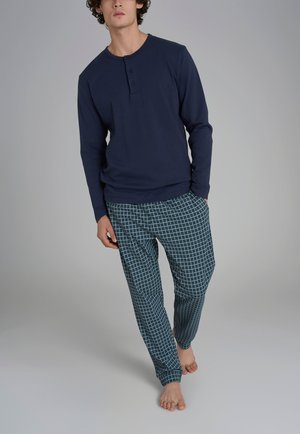 Maglietta henley a maniche lunghe di colore blu navy con tre bottoni, abbinata a pantaloni da pigiama a scacchi verdi, dotati di una cintura elastica e polsini alla caviglia.