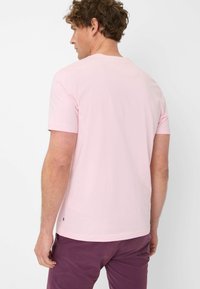 T-shirt rosa chiaro a maniche corte realizzato in tessuto morbido, con scollatura rotonda e un piccolo etichetta logo in basso a sinistra.