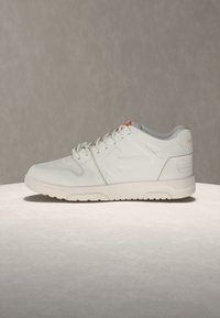 Λευκό sneaker χαμηλής κορυφής με κορδόνια, χοντρή σόλα και λεπτές σχεδιαστικές λεπτομέρειες σε ουδέτερο φόντο.