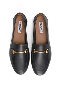 Mocasines de piel negra con un acento de cadena dorada en el empeine, textura suave, punta redondeada y un interior acolchado.