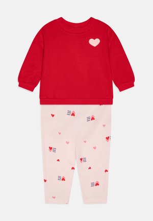 Crvena dukserica s malim bijelim srcem na prsima, u kombinaciji s ružičastim hlačama koje imaju razne veličine crvenih srca i uzorak teksta "XOXO".