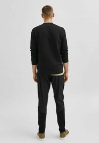 Černý textured svetr s dlouhými rukávy, zkombinovaný s černými kalhotami s kontrastními látkovými panely a světle hnědými botami.