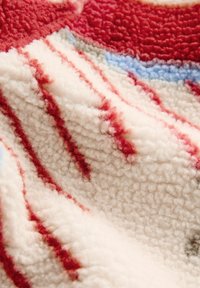 Tissu polaire doux avec une surface texturée en blanc, rouge et bleu disposés en motifs abstraits.