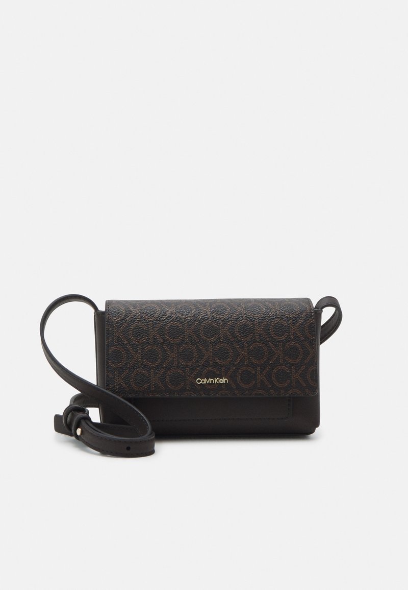Pequeña bolsa tipo bandolera con correa ajustable, tapa de cuero marrón impresa con el logo repetido de CK y el branding dorado de Calvin Klein en la parte delantera.