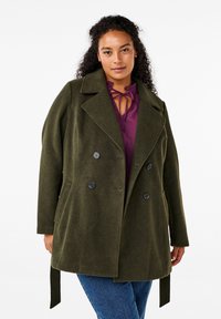 Cappotto in misto lana verde oliva con design doppiopetto, rever a punte e bottoni neri. Include tasche laterali e un dettaglio con cintura.