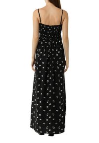 Zwart maxi-jurk met witte abstracte patronen, met verstelbare schouderbanden en een gerimpelde corsage. Zachte, lichte stof met een vloeiende silhouet.