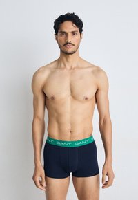 Tengerészkék boxer alsónadrág zöld elasztikus derékkal, amin a „GANT” logó található. Puha, rugalmas anyag és testhezálló kialakítás.