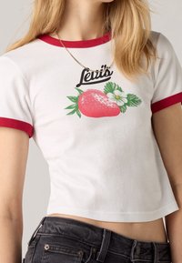 Camiseta corta de manga corta blanca con ribete rojo, que presenta un gráfico de una fresa y hojas, acompañado del logo de "Levi's".