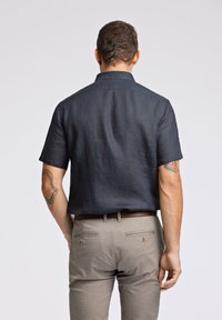 Camicetta a maniche corte in lino blu scuro con colletto, abbinata a pantaloni texture grigi chiari con due tasche posteriori e dettagli con bottoni.