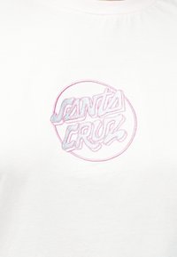 Balta T-krekls ar pasteļrozā un zila izšūtu "Santa Cruz" logotipu apļa formā uz krūšu daļas. Mīksta kokvilnas tekstūra.