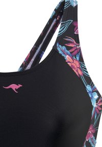 Haut de bain noir avec un motif floral en rose, bleu et vert. Possède des bretelles larges et un petit logo kangourou rose sur le côté gauche.