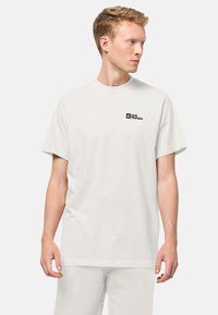 Weißes Baumwoll-T-Shirt mit kurzen Ärmeln und Rundhalsausschnitt, mit einem schwarzen rechteckigen Logo auf der linken Brustseite. Einfaches und minimalistisches Design.