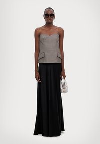 Grijze strapless top met peplum-detail, gecombineerd met een lange zwarte satijnen rok. Model houdt een kleine zilveren handtas vast en draagt een zonnebril.