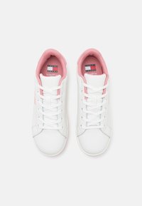 White sneakers with pink accents and laces. Smooth synthetic material, rounded toe, padded collar, and branded insole detailing.