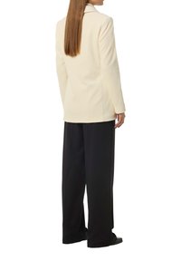 Cremefarbener gerippter Blazer mit Reverskragen, kombiniert mit lockeren schwarzen Hosen. Der Blazer verfügt über gesteppte Akzente und eine taillierte Passform.