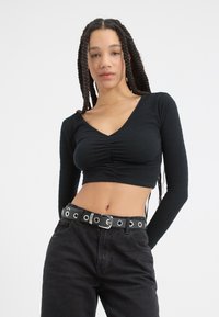 Svart cropped langermet topp med v-hals, teksturert stoff og rynkete detaljer, sammen med høyt liv svarte jeans og et naglet belte.