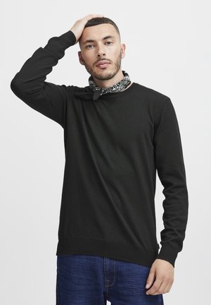 Black knitted sweater with long sleeves and crew neckline. Features ribbed cuffs and hem. Styled with a black and white patterned scarf.