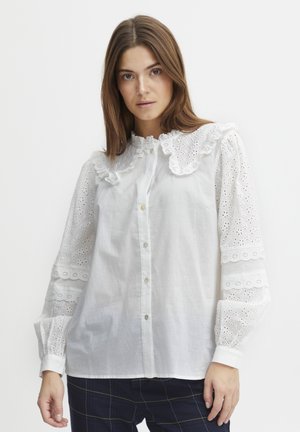 Weiße Bluse mit Rüschensaum am Kragen und bestickten Details an den Ärmeln. Knopfleiste vorne mit klassischer Passform und geknöpften Ärmeln.