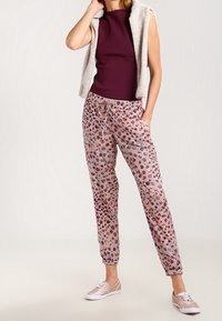 Lekka, różowa para dresowych spodni w wzory, z elastycznym pasem i mankietami. W zestawie z dopasowanym, bezrękawnikowym, ciemnofioletowym topem i jasnym obuwiem.