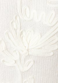 Weißer gestrickter Stoff mit erhabenen Blumen- und Schriftmustern, die durch strukturierte Stiche erzeugt werden.