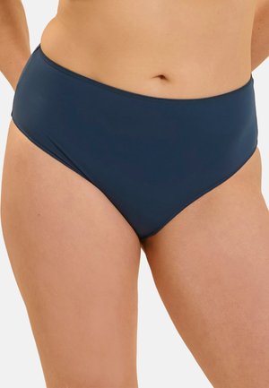 Frau trägt dunkelblaue hoch taillierte Bikinihose, gezeigt vom mittleren Oberkörper bis zu den oberen Oberschenkeln vor einem einfarbigen Hintergrund.