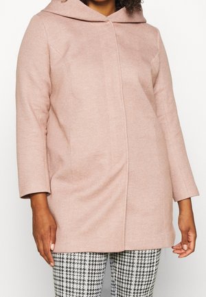 Mujer con abrigo con capucha de color rosa claro con mangas largas combinado con pantalones de estampado pata de gallo en blanco y negro.