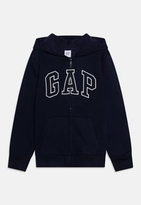 Mornarsko plava majica s patentnim zatvaračem, izrađena od mekog pamuka, s velikim bijelim logotipom "GAP", kengur žepovima i kapuljačom s vezicom.