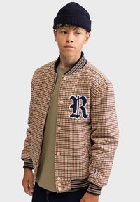 Houndstooth-patterned, brown and beige jacket with navy ribbed collar and cuffs, featuring a navy embroidered "R" logo, brass snap buttons.