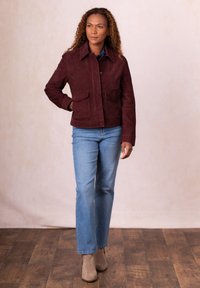 Burgundy suede jacket with a collar, two front pockets, and a snap closure, paired with light blue jeans and beige ankle boots.