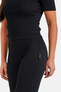 Ensemble de sport noir avec un motif texturé. Haut à manches courtes avec col rond associé à des leggings texturés taille haute, étiquette logo sur le côté.