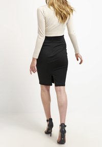 Svart blyertskjol med en slits bak, ihopparad med en fitted creamfärgad långärmad topp. Modellen bär svarta högklackade skor.