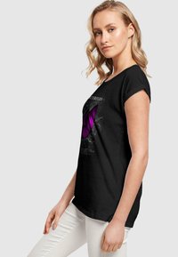 Black cotton T-shirt featuring a purple butterfly graphic with text. Short sleeves and a relaxed fit design, worn with white pants.