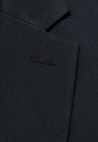 Sort stof med en glat tekstur, der har en lille syning på kraven af en blazer. Stoffet er fint vævet og ensartet i farven.