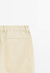 Pantalon beige avec taille élastique, texture lisse et poche arrière simple. Design simple et ajusté avec des accents cousus.