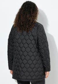 Černá prošívaná péřová bunda s diamantovým vzorem, dlouhými rukávy a volným střihem. Hladká textura, kulatý výstřih a střední délka.