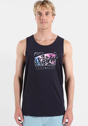 Homme portant un débardeur noir avec un logo coloré "OXBOW SURF GEAR", debout devant un fond clair uni.