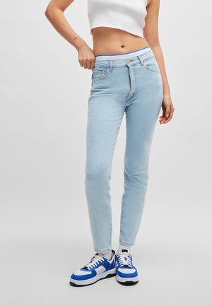 Lichtblauwe skinny jeans met hoge taille, voorzien van zijzakken en een blauwe accent op de tailleband, gecombineerd met blauw-witte sneakers.