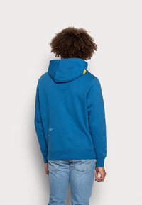 Blå hoodie med snörning i huvan, med en gul accent. Tillverkad av mjukt, texturerat tyg, har den en avslappnad passform och ribbade ärmslut.