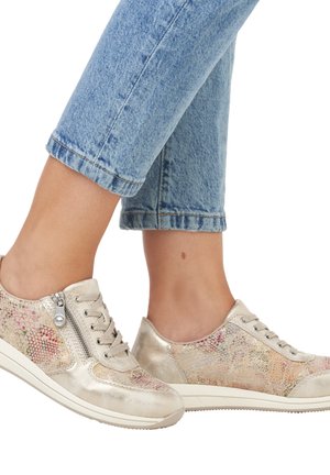 Metaliczne złote sneakersy z teksturowanym, wielokolorowym wzorem; z sznurówkami i bocznym zamkiem; zestawione z podwiniętymi niebieskimi dżinsami.