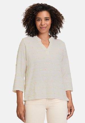 Blouse beige clair avec un décolleté en V, ornée de détails rayés colorés en rose fluo et vert. Fabriquée en tissu texturé, à manches trois-quarts.