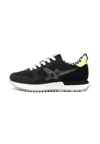 Sneaker nera con lacci bianchi, con logo argentato scintillante, dettagli verde lime, particolari in suede e suola in gomma testurizzata con un motivo a zigzag.