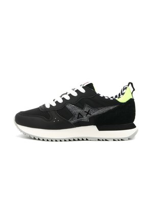 Sneaker nera con lacci bianchi, con logo argentato scintillante, dettagli verde lime, particolari in suede e suola in gomma testurizzata con un motivo a zigzag.