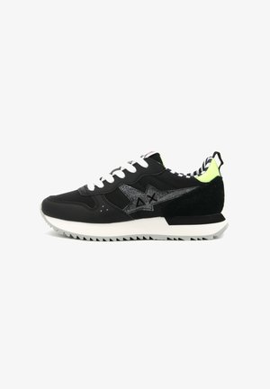 Sneaker nera con lacci bianchi, con logo argentato scintillante, dettagli verde lime, particolari in suede e suola in gomma testurizzata con un motivo a zigzag.
